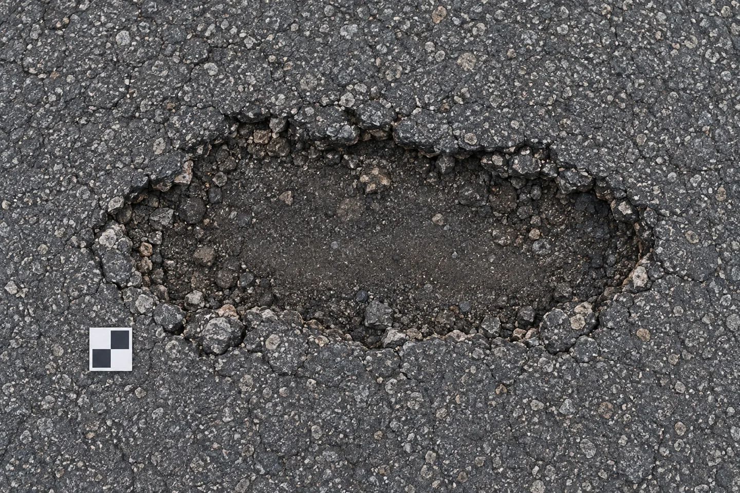 Ilustración cenital de un bache sobre asfalto, con una tarjeta de escala a un lado